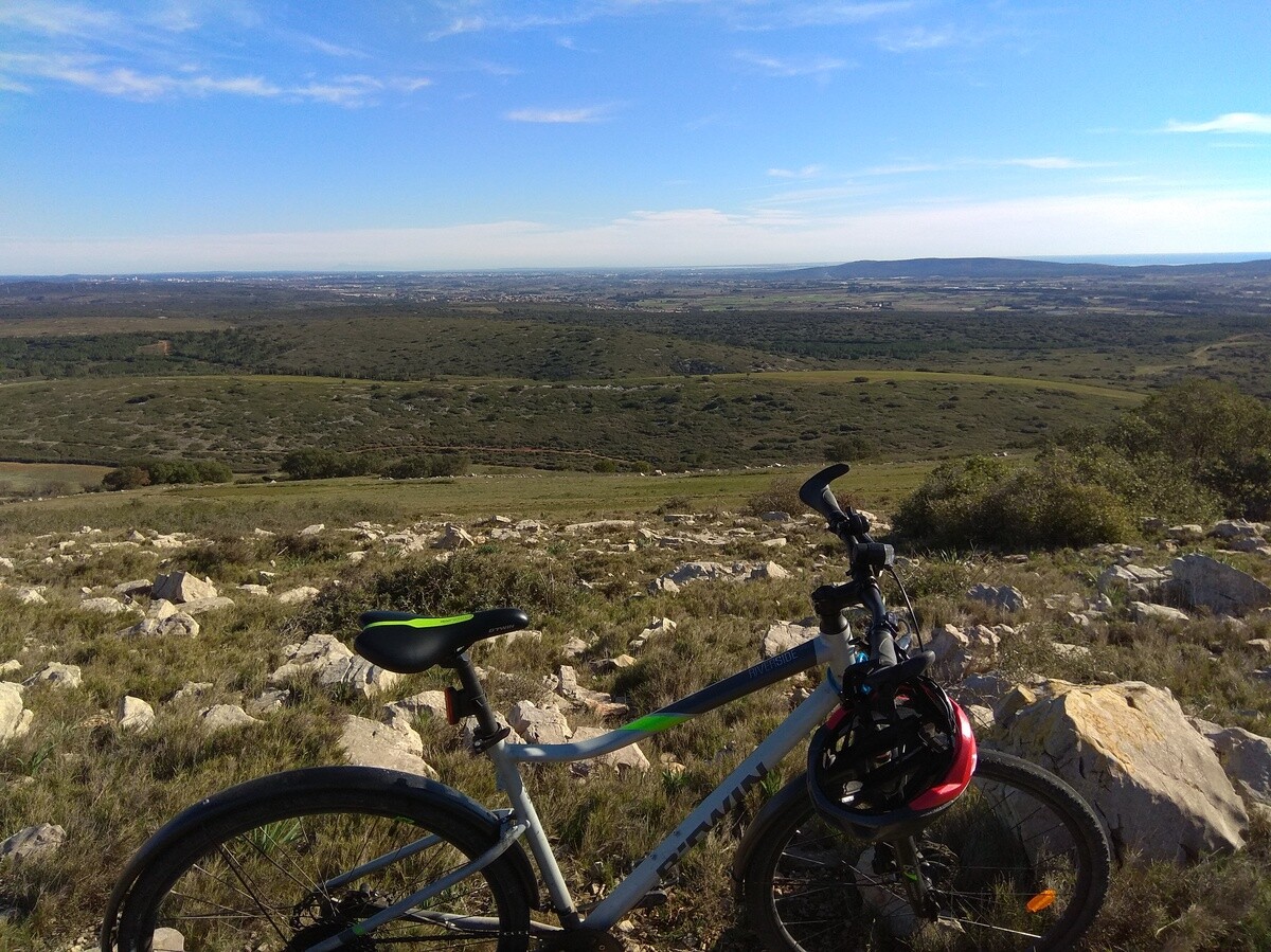 Un vélo posé. Derrière la vue s'étend sur une plaine. Photo prise depuis les hauteurs d'un causse.