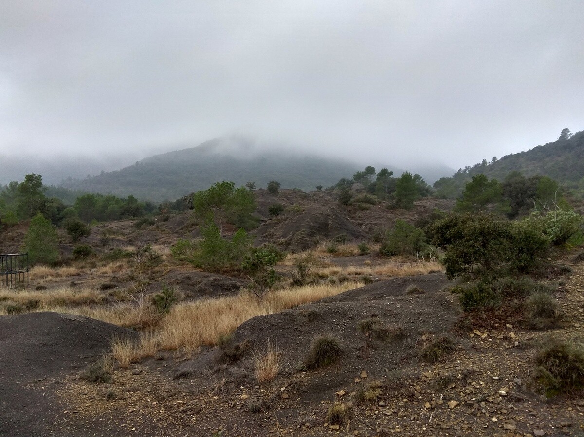 Une étendue marneuse au pied d'un massif karstique sous un épais brouillard.