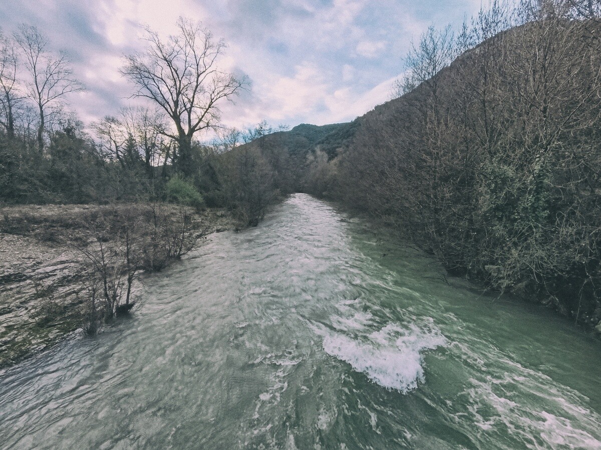 Un petit fleuve à l'eau tumultueuse passe entre une rive rocheuse et des arbres.